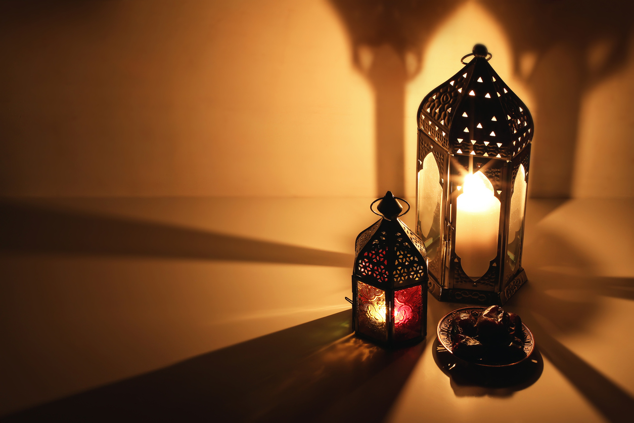 Ornamental Arabic lanterns, burning candles glowing at night. Plate with date fruit on the table. Golden festive greeting card, invitation for Muslim Ramadan Kareem holiday, iftar dinner background.