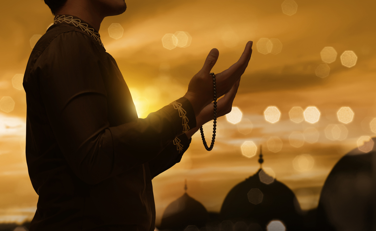 Muslim man raising hand and praying with prayer beads during sunset background